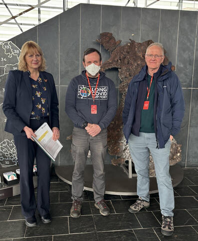 Masked advocate at the Welsh Senedd standing with two other people
